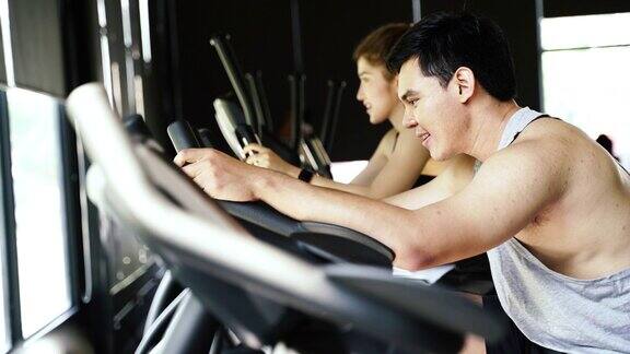侧面的亚洲女人和男人在健身房骑动感单车年轻夫妇一起锻炼和做有氧运动