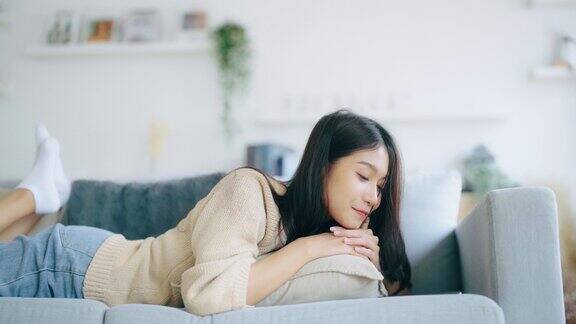 快乐的年轻亚洲女性在家里放松女人笑着躺在沙发上手里拿着手机女孩用视频打电话给朋友
