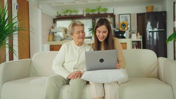 年轻的亚洲女人和她的祖母坐在客厅里使用笔记本电脑