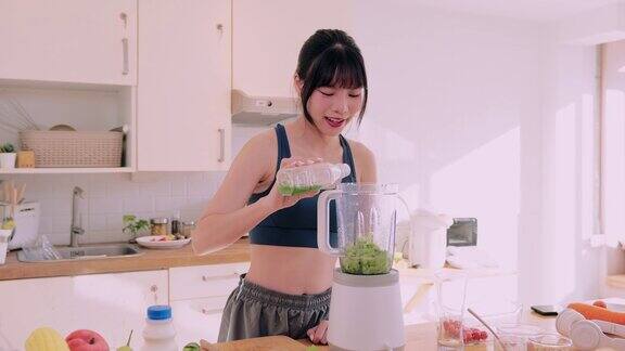 一位穿着运动服的快乐的亚洲妇女将水果和蔬菜混合在一起在她的厨房里品尝着营养丰富的冰沙她崇尚健康快乐的生活方式提倡健康饮食的好处