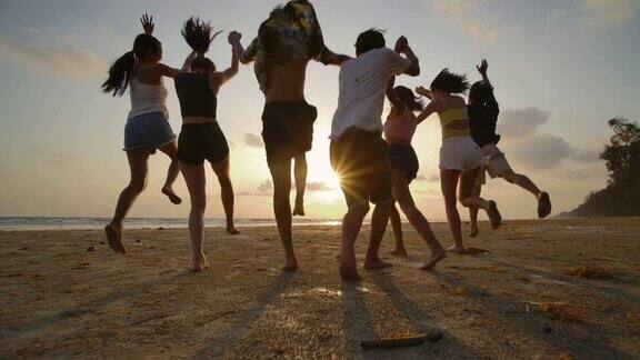 慢镜头-日落时分一群朋友在海滩上奔跑心情愉快有聚会庆祝观念的人后视图