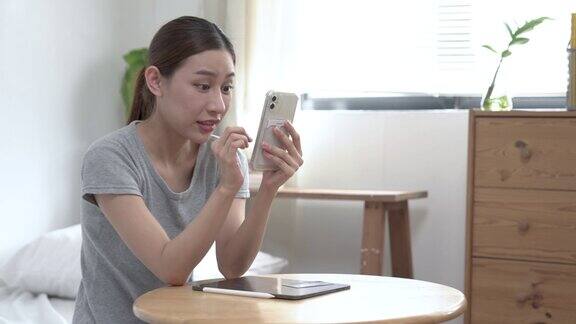 幸福的亚洲女性拿着信用卡在家里的卧室里用智能手机在线购物