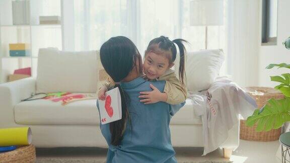 年轻的亚洲家庭的妈妈和女儿拥抱和阅读亲手制作的贺卡在家里庆祝母亲节在客厅里玩得很开心家庭幸福时刻