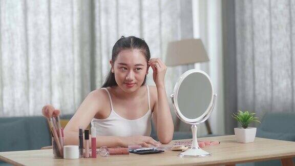 年轻美丽的亚洲女人微笑着看着镜子里的头发准备在家里化妆