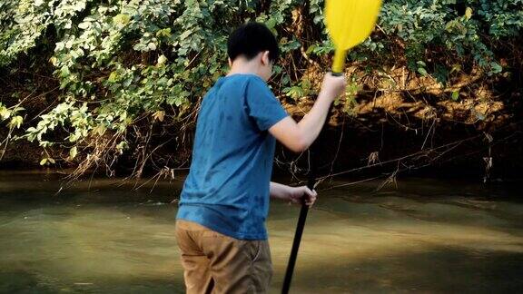 亚洲男孩抱着桨在河里早上生活方式
