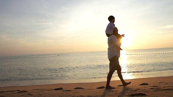 日出时父亲和儿子在海滩上散步他们一起度过了宝贵的家庭时光用慢镜头拍摄