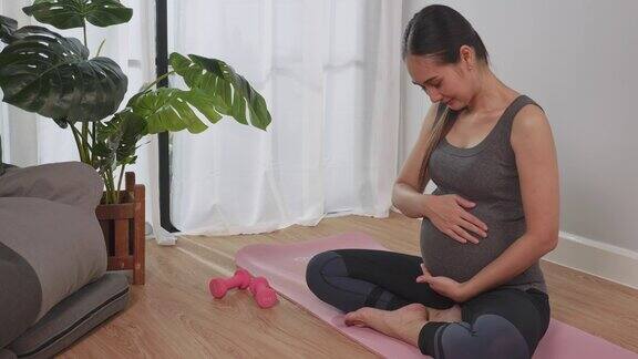一位穿着运动服的亚洲孕妇在家里运动时深情地抚摸着她未出生的孩子