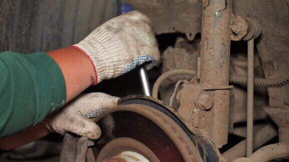 一个男人在车间里修理他的汽车刹车盘一个人拧开了紧固件换上了一个新的部件用自己的双手修理刹车盘