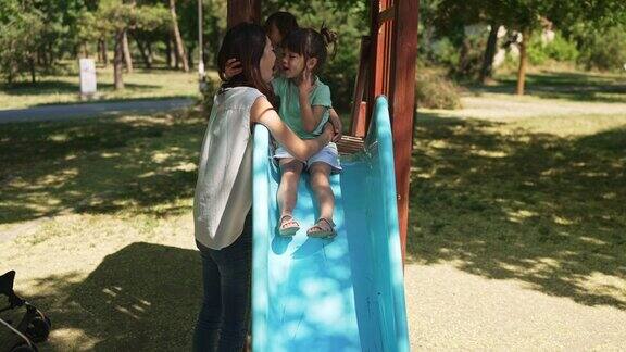 小女孩抱着妈妈站在公园的滑梯上