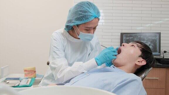 亚洲女牙医在牙科诊所检查年轻男性病人的牙齿