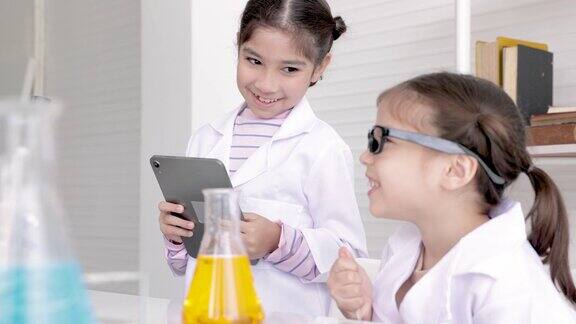 可爱的小学女生穿着实验服在学校实验室学习化学用记事本技术记录例子和分析在科学课上混合液体教育和科学概念