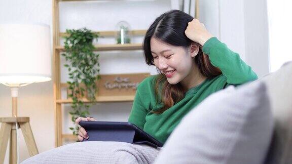 亚洲女性在客厅使用平板电脑同时在家里的沙发上放松