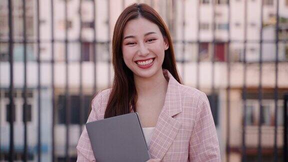 年轻的亚洲女商人拿着笔记本电脑微笑着看着相机