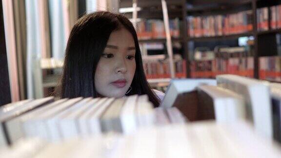 亚洲女学生在大学图书馆的书架上看书教育