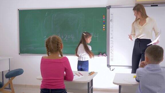 小学数学课上女学生在教师旁边的黑板上写一个简单的例子