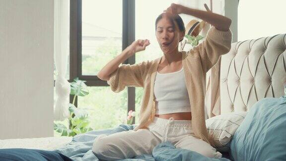 亚洲女孩穿着白色的奶油睡衣开襟羊毛衫在毛茸茸的舒适的床上快乐地跳舞在家里的卧室里度过了漫长的假期女性早晨的感觉
