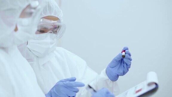 冠状病毒大流行期间两名身穿防护服的医务人员在剪贴板上讨论血液检测结果