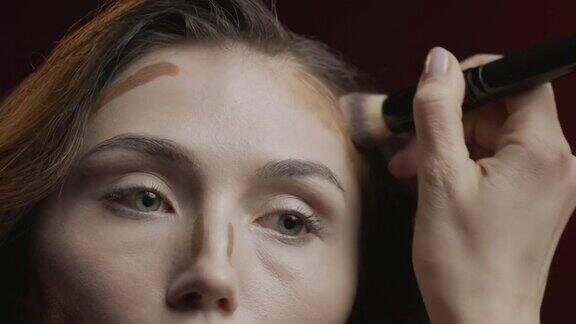 化妆的步骤一个女人用化妆刷在额头上涂抹深色遮瑕膏的特写