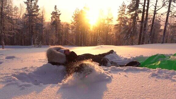 慢镜头:金色的夕阳下快乐的女孩在山上的雪地里制作雪天使