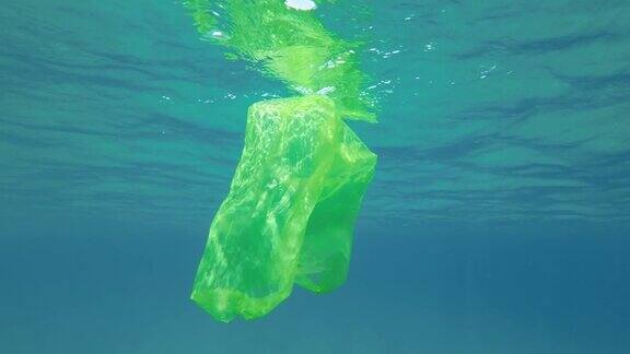 慢动作黄色的塑料袋在水下游泳反射在阳光下蓝色的水面上废弃的塑料袋在阳光下慢慢漂浮在水面下塑料污染
