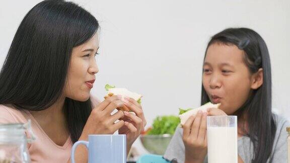 慢镜头亚洲母女坐在家里的厨房里吃着三明治脸上带着幸福的笑容