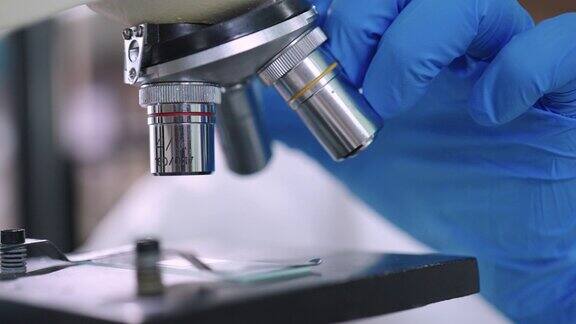 科学家的手在实验室的显微镜下使用样本的特写