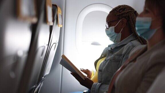 一名非洲成年女性戴着口罩在飞机上看书以应对新冠肺炎疫情
