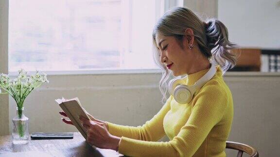 快乐的年轻亚洲女子在家里客厅的桌子上看书
