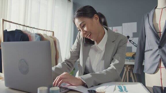 专业开朗的亚洲女商人设计师坐在办公桌上用笔记本电脑打电话给客户在工作室工作场所的网上市场确认购买订单成功的事业