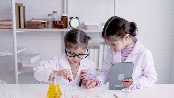 4K两个亚洲女孩站在科学教室里做化学实验他们两个人互相帮助做实验从一个玻璃烧瓶里挤水到烧杯里实验