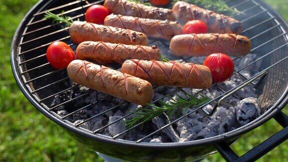 烤香肠在草地上的圆形烤架上烤香肠配上西红柿和迷迭香夏季户外野餐
