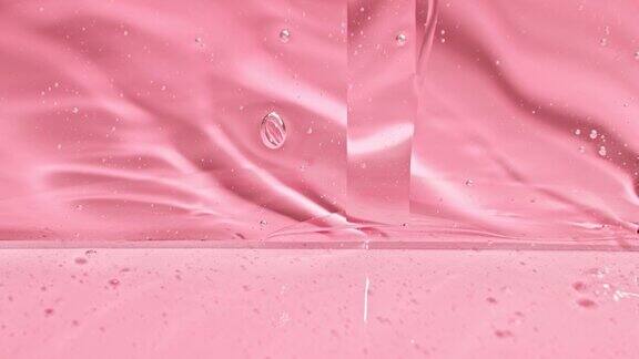 透明的化妆品液体凝胶霜慢慢滴在粉红色的背景下流动