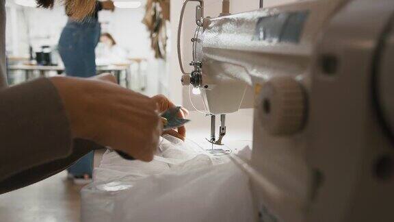 在车间工作的女裁缝在缝纫机上缝制薄纱和用剪刀剪线的双手
