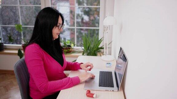 一名妇女在家用笔记本电脑工作时使用哮喘吸入器