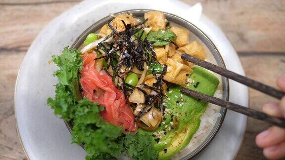 俯视图:筷子从一个素食碗里夹一块豆腐里面有海藻、西瓜萝卜、毛豆和牛油果健康素食午餐