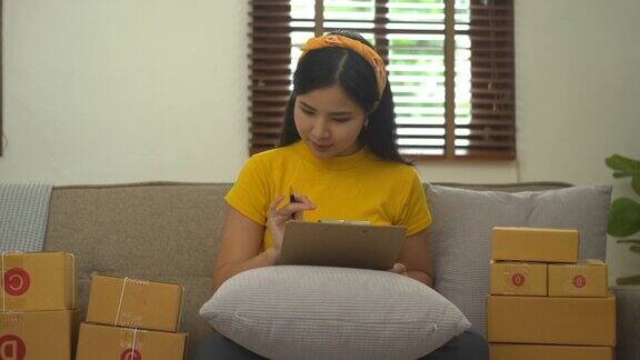 启动中小企业亚洲妇女与包装盒工作而坐在沙发上