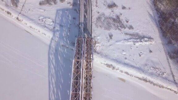 铁路桥为铁路交通在冬季河流上的雪景无人机视图悬索桥通过冬季河流和铁路轨道鸟瞰图