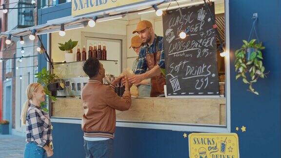 快餐车员工给一个穿着皮夹克的快乐年轻人分发一个汉堡印度男子使用非接触式银行借记卡购买食物街头快餐车在户外卖汉堡