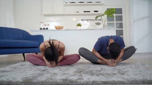一对亚洲夫妇在家里的客厅里练习瑜伽姿势