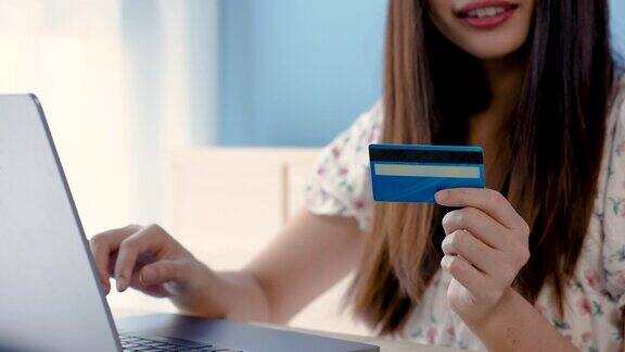 4K50fps美丽的亚洲女孩美丽的亚洲女孩穿着白色花衬衫通过笔记本电脑在线支付订单他的手拿信用卡网上购物