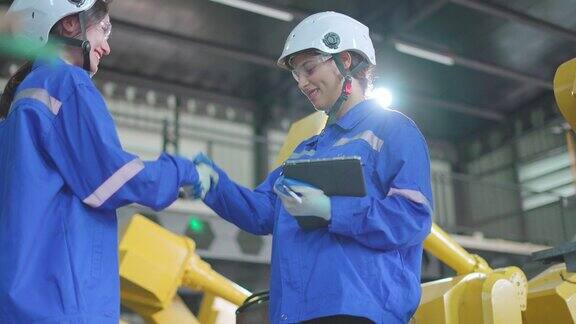 女经理与在生产线上一起工作的工程师或技术人员握手团队机械师戴安全帽在工厂从事机械臂的专业维修工作自动化制造工业技术