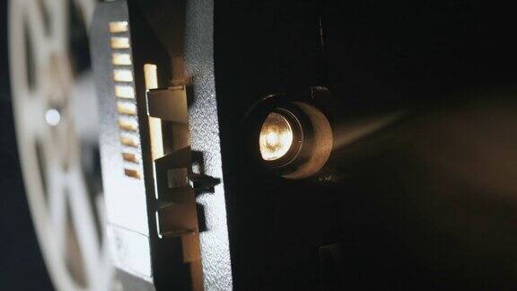 一个老式的古董超级8毫米电影放映机的正面视图投射一束光在一个黑暗的房间旁边的一堆散开的电影