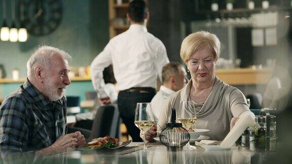 餐厅服务员为坐在餐桌旁的老夫妇上菜