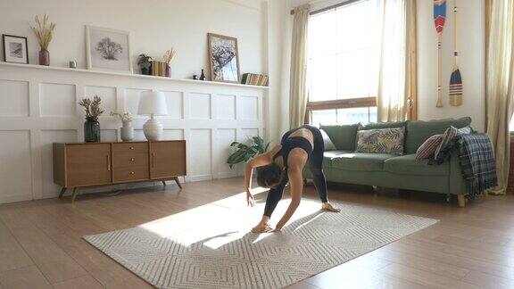 一个穿着紧身裤和t恤的女人在阳光明媚的早晨在客厅里做瑜伽姿势