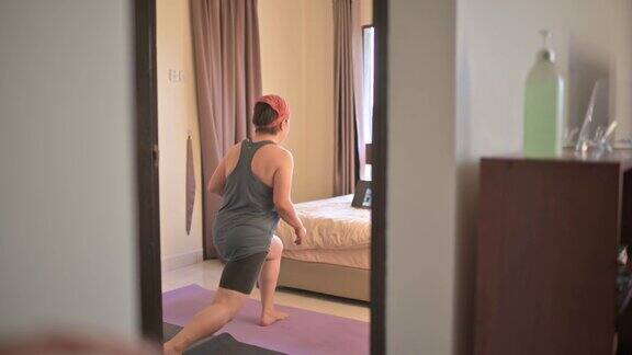 后视图亚洲华人中年妇女戴头巾在家锻炼锻炼在线学习健身教练通过智能手机在卧室在晚上