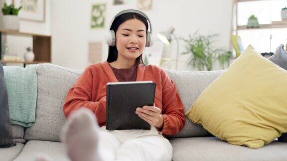 快乐的女人平板电脑或音乐耳机在家庭沙发上播放流媒体电影有趣的节目或电子竞技游戏微笑亚洲或放松的学生在科技互联网博客或社交媒体上听耳机