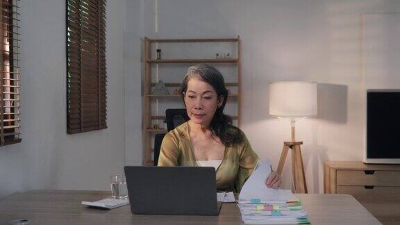 亚洲老年妇女在家时在电脑桌上处理文件