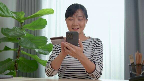 亚洲女性手持信用卡在家里用智能手机网购