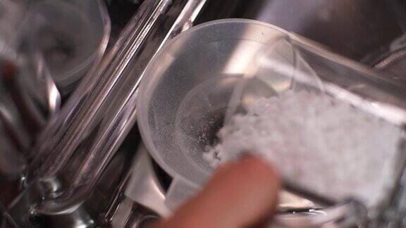 不知名的家庭主妇将漏斗插入洗碗机的孔中并倒入颗粒盐来软化硬水