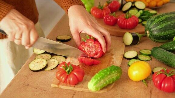 一个女人正在用刀切新鲜的生蔬菜西红柿、黄瓜在木板上切成片在家里做一顿健康的素食餐准备素菜的切食材4K